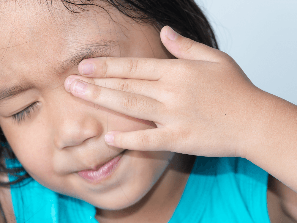 Criança cobre um dos olhos com a mão, sugerindo desconforto visual que pode estar associado ao hábito de piscar em excesso.